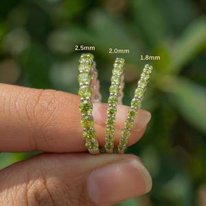 May include: Three silver rings with a row of small, round, light green gemstones. The rings are labeled with sizes: 2.5mm, 2.0mm, and 1.8mm. The background is a soft green, suggesting a natural setting.
