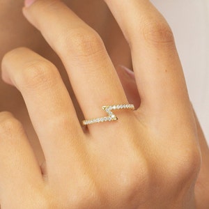 May include: A gold ring with a lightning bolt design set with small clear stones.