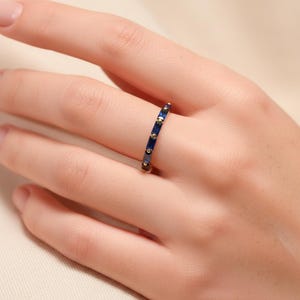 May include: A gold-toned ring with a band of alternating dark blue rectangular stones and small gold-colored dots. The ring is worn on a finger, showcasing its design and color contrast. The ring is a piece of jewelry.