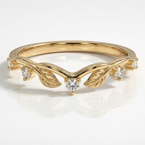 May include: A gold ring with a leaf design. The ring features small, clear gemstones and leaf-shaped accents. The ring's band is smooth and polished, and the overall design is elegant and nature-inspired.