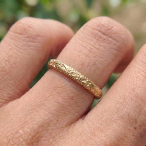 Op de afbeelding: Een goudkleurige ring met een bloemmotief. De ring wordt om een vinger gedragen en het ingewikkelde ontwerp is zichtbaar. Het oppervlak van de ring is getextureerd met gedetailleerde gravures van bloemen en bladeren, wat een delicate en elegante uitstraling creëert. De ring is een sieraad.