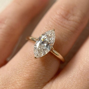 May include: A marquise-cut diamond ring with a gold band. The diamond is set with four prongs, and the band is a simple, polished gold. The ring is shown on a finger.