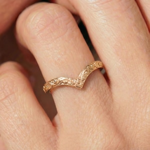 Può includere: Un anello a forma di V color oro con un intricato motivo floreale. L'anello è curvo e si adatta al dito. Il design dell'anello presenta intagli dettagliati di fiori e foglie, creando un aspetto delicato e ornato.