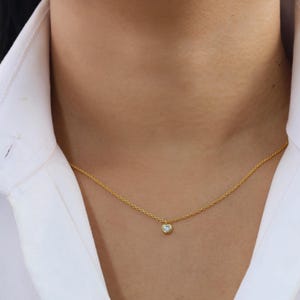 May include: A delicate gold chain necklace with a small, clear gemstone pendant.