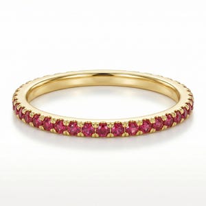 May include: A gold band ring set with a continuous row of vibrant red gemstones. The ring's polished gold setting provides a striking contrast to the rich color of the gemstones, creating a classic and elegant design.