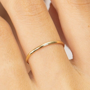 May include: A simple gold band ring worn on a finger.
