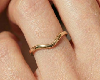 May include: A polished gold ring with a smooth, continuous wave-like design that curves gently along the band. The metal has a reflective, high-shine finish, and the ring features a simple, minimalist silhouette that sits flush against the finger.