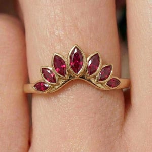 Op de afbeelding: Een goudkleurige ring met een kroonvormig ontwerp, bezet met dieprode, marquise-geslepen edelstenen. De ringband is van gepolijst goud. De edelstenen zijn dicht op elkaar geplaatst.