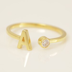 May include: A gold ring featuring a letter 'A' and a small clear stone.