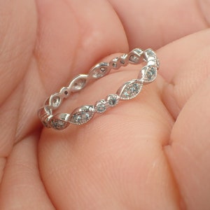 May include: A silver band ring with a delicate design of small, clear stones set in a scalloped pattern.