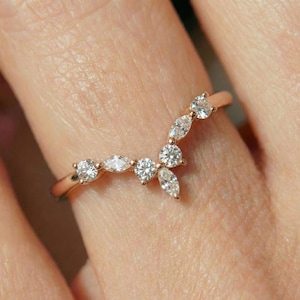 Pode incluir: Um anel de ouro rosa com um design curvo, cravejado com vários diamantes claros e brilhantes. Os diamantes são de corte redondo e marquesa, criando uma aparência delicada e elegante. O anel é mostrado em um dedo.