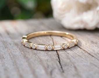 May include: A gold band ring featuring an alternating pattern of clear baguette-cut and round-cut stones set along the top half of the band. The metal has a polished finish, and the stones are arranged in a repeating sequence of one baguette and one round.
