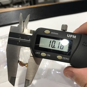 May include: A black digital caliper measuring 10.16 inches. The caliper has a black display with white numbers, and the words "in/mm" and "UPM" are printed on the display.