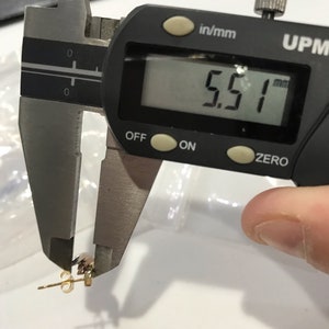 May include: A close-up of a digital caliper measuring a small gold earring. The caliper reads 5.51 mm.