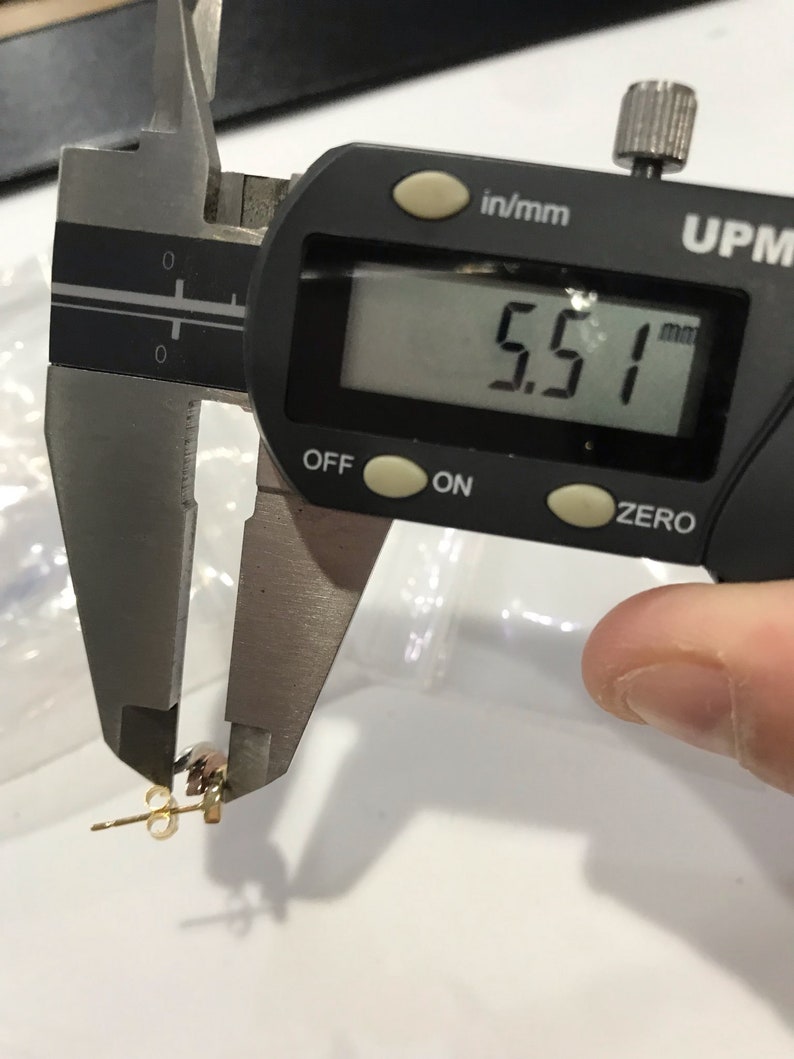 May include: A close-up of a digital caliper measuring a small gold earring. The caliper reads 5.51 mm.