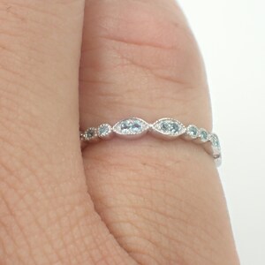 May include: A delicate silver band ring with a row of small, oval-shaped blue gemstones.