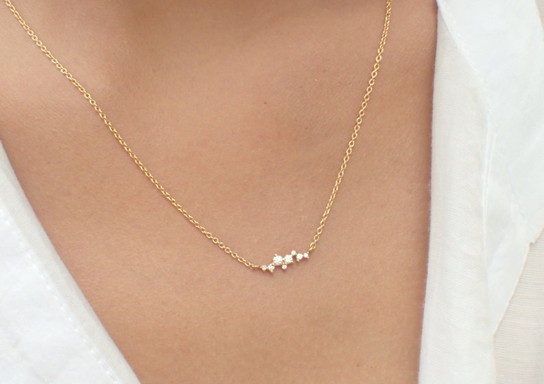 May include: A delicate gold chain necklace with a small cluster of sparkling diamonds in a curved line design.
