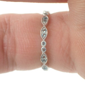 May include: A delicate silver band ring with a row of small, light blue gemstones set in a scalloped design.