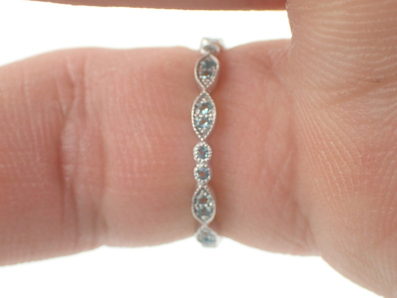May include: A delicate silver band ring with a row of small, light blue gemstones set in a scalloped design.
