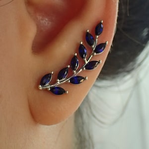 May include: A silver ear cuff with a delicate branch design featuring dark blue marquise-shaped gemstones.