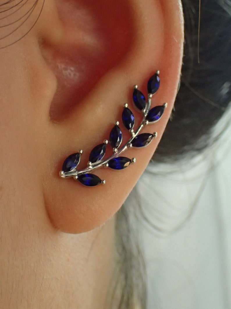 May include: A silver ear cuff with a delicate branch design featuring dark blue marquise-shaped gemstones.