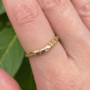 May include: A gold curved band ring featuring a series of small, round, yellow gemstones set along one side. The metal surface is polished and decorated with engraved star motifs that surround the stones, creating a celestial-inspired design.