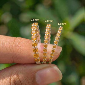 Könnte beinhalten: Drei zarte Ringe mit gelben Edelsteinen werden gezeigt. Die Ringe sind mit Größen beschriftet: 2,5 mm, 2,0 mm und 1,8 mm. Die Edelsteine sind in einem silbernen Band gefasst. Der Hintergrund ist ein sanftes Grün.