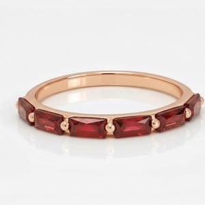 Puede incluir: Anillo de oro rosa con piedras preciosas rectangulares de color rojo intenso. La banda del anillo es de un color metálico cálido, y las piedras preciosas están espaciadas uniformemente. Las piedras preciosas son de un color rojo vibrante y saturado.