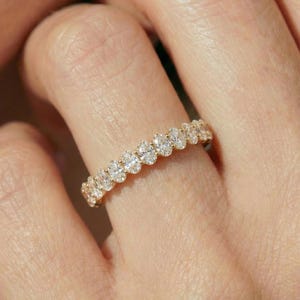 May include: A gold ring with a continuous row of oval-shaped diamonds. The ring is set in a yellow gold band and is worn on a finger. The diamonds sparkle, reflecting light. The ring is a piece of jewelry.