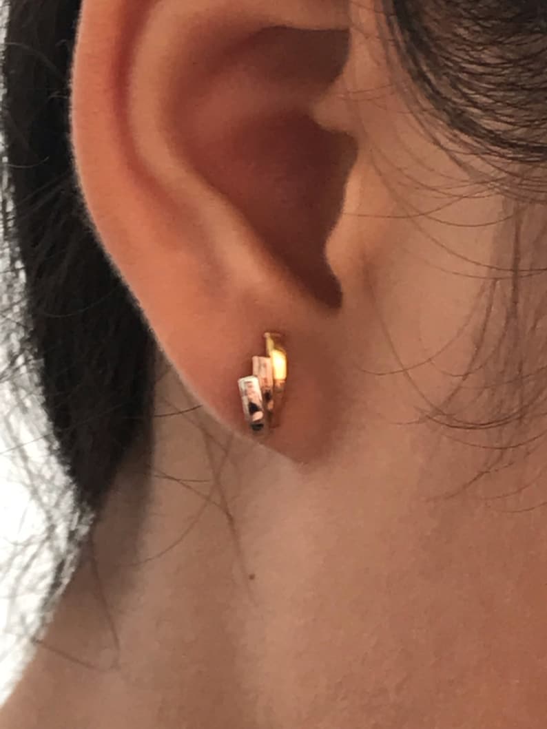 May include: A close-up of a person's ear with a gold hoop earring. The earring is made of multiple thin hoops stacked on top of each other.