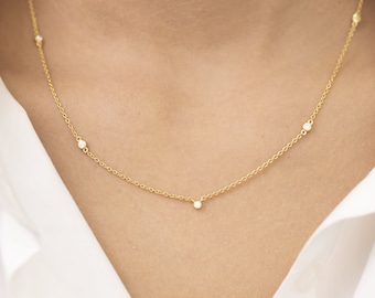 May include: A delicate gold chain necklace with five small, clear gemstones.