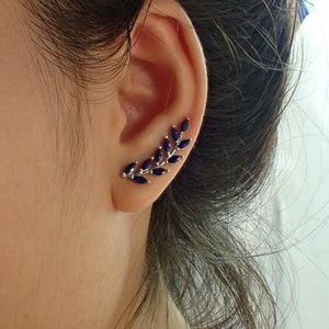 May include: A silver ear cuff with a delicate branch design featuring dark blue gemstones. The cuff is worn on the upper part of the ear.