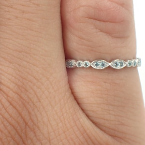 May include: A delicate silver band ring with a row of small, light blue gemstones set in a scalloped design.