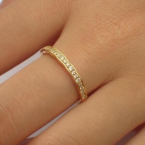 Pu&ograve; includere: Un anello dorato con un design ondulato, incastonato con piccole pietre preziose trasparenti. L'anello &egrave; indossato su un dito, mostrando il suo aspetto delicato ed elegante. Le pietre preziose sono uniformemente distanziate lungo la parte superiore dell'anello.