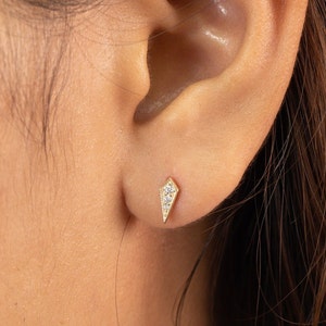 Op de afbeelding: Een paar gouden oorbellen met een diamantvormig ontwerp. De oorbellen zijn klein en delicaat en hebben elk een enkele diamant in het midden.