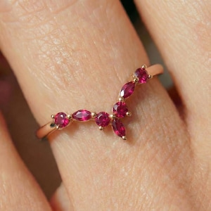 May include: A gold ring featuring a curved design adorned with multiple vibrant red gemstones. The ring's band is a warm gold color, and the gemstones are a deep, rich red, creating a striking contrast.