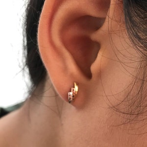 May include: A close-up of a person's ear with a gold hoop earring. The earring has a unique design with multiple layers of gold.