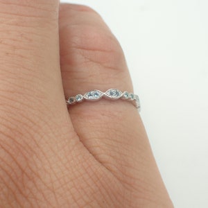 May include: A delicate silver band ring with a row of small, oval-shaped blue gemstones.