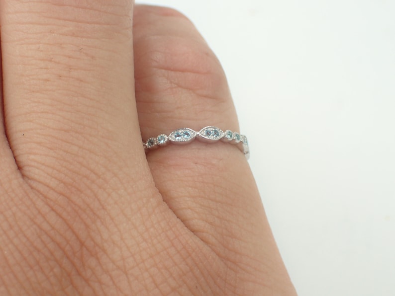 May include: A delicate silver band ring with a row of small, oval-shaped blue gemstones.