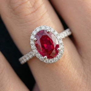 May include: A dazzling engagement ring featuring a large, oval-cut ruby gemstone surrounded by a halo of smaller, sparkling diamonds. The ring's band is also encrusted with diamonds, creating a brilliant display of light and color.