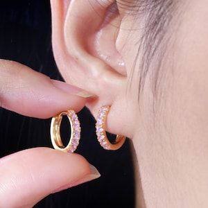 May include: A pair of gold hoop earrings with pink cubic zirconia stones. The earrings are small and delicate.
