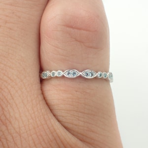 May include: A delicate silver band ring with a row of small, light blue gemstones set in a scalloped design.
