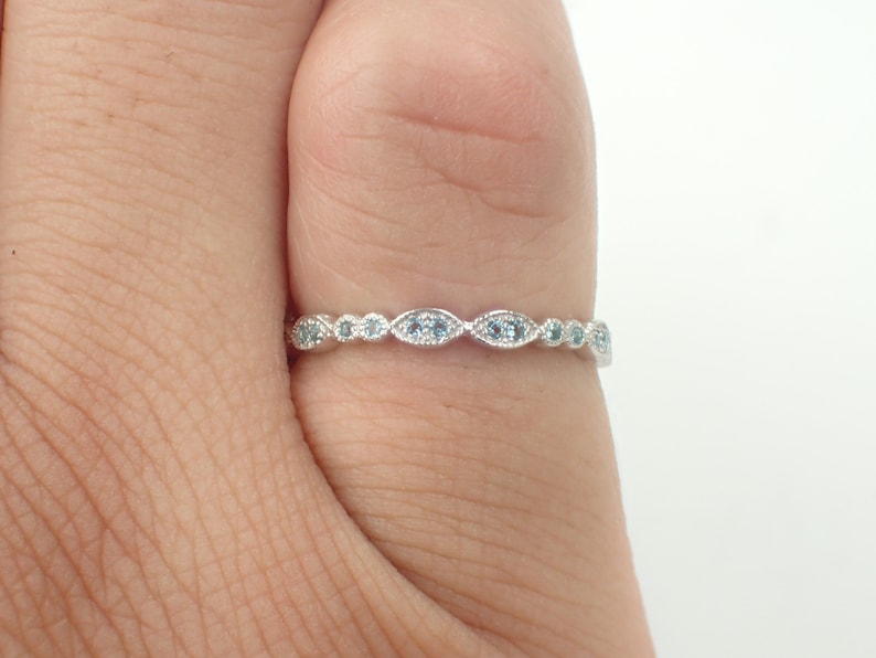 May include: A delicate silver band ring with a row of small, light blue gemstones set in a scalloped design.