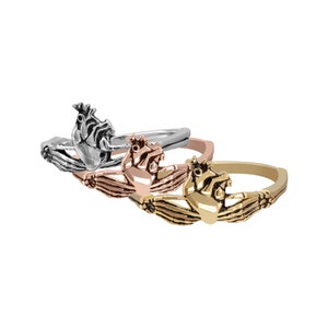 Puede incluir: Tres anillos de Claddagh en plata, oro rosa y oro. Cada anillo presenta un coraz&oacute;n sostenido por dos manos, coronado por una corona. Los anillos se muestran sobre un fondo blanco.
