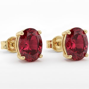 Pode incluir: Um par de brincos de ouro com tachas, cada um com uma pedra preciosa vermelha oval vibrante. As pedras são fixadas em uma configuração de quatro garras, com um design clássico e elegante.