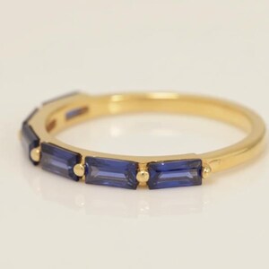 May include: A gold ring with a band of rectangular, deep blue gemstones. The ring's gold band is smooth and polished, with the blue stones set in a row around the top. The gemstones are a vibrant, saturated blue.