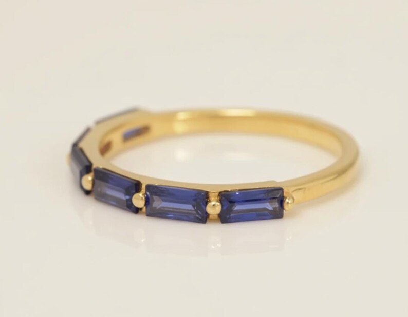 May include: A gold ring with a band of rectangular, deep blue gemstones. The ring's gold band is smooth and polished, with the blue stones set in a row around the top. The gemstones are a vibrant, saturated blue.