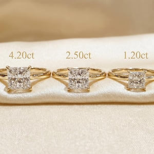 May include: Three gold rings with square-cut diamonds of varying sizes: 4.20ct, 2.50ct, and 1.20ct. The rings are displayed on a cream-colored satin surface, showcasing the brilliance of the gemstones.