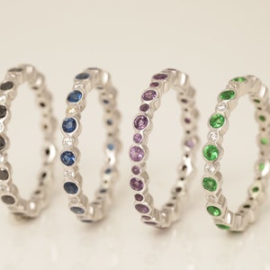 May include: Four silver rings with a row of colorful gemstones. The rings feature black, blue, purple, and green gemstones.
