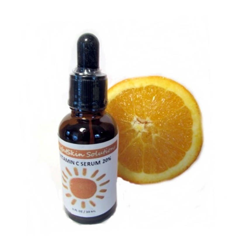 Puede incluir: Una botella de vidrio marr&oacute;n de s&eacute;rum de vitamina C con un cuentagotas negro, junto a una rodaja de naranja. La etiqueta dice "Skin Solutions Vitamin C Serum 20%" con un sol. Contiene 30 ml.